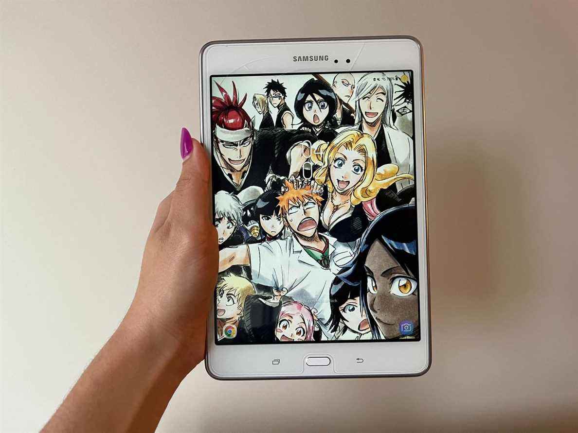 Une main de femme avec des ongles peints en rose tenant une tablette avec des personnages d'anime sur le devant.