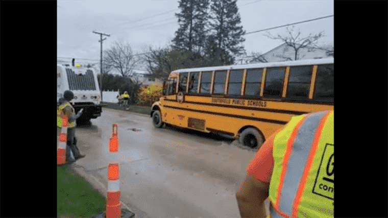 Regardez un autobus scolaire traverser le béton mouillé avec des enfants à bord