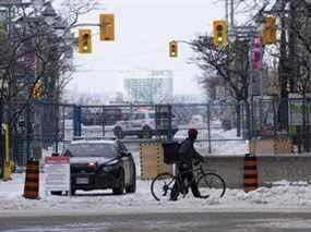 Un cycliste pousse son vélo à travers une intersection devant une clôture temporaire sous le regard de la police depuis sa voiture le 23 février 2022 à Ottawa.