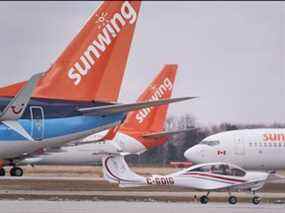 Un petit avion passe devant des Boeing 737 appartenant au transporteur aérien Canadian Vacation Sunwing assis sur le tarmac de l'aéroport international de Waterloo à Waterloo, en Ontario, le 24 mars 2020.