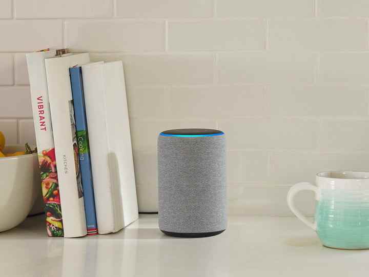 Un Amazon Echo sur une table entre quelques livres et une tasse de café.