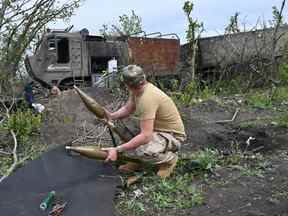 Un militaire ukrainien inspecte une munition abandonnée à côté d'un véhicule militaire russe détruit près du village de Mala Rogan à l'est de Kharkiv, le 13 mai 2022, au milieu de l'invasion russe de l'Ukraine.