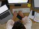 Une femme travaille sur un ordinateur de bureau à côté d'un ordinateur portable Apple Inc. dans un bureau à domicile.