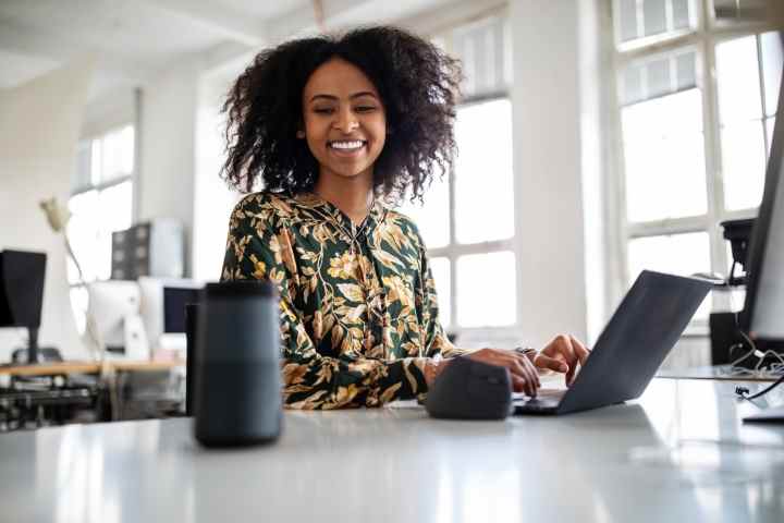 Femme utilisant un haut-parleur intelligent tout en travaillant au bureau.