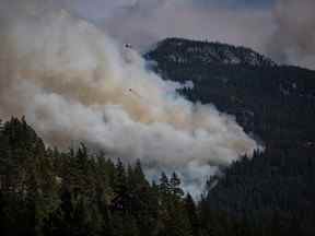 Un hélicoptère transportant un seau d'eau survole le feu de forêt de Lytton Creek qui brûle dans les montagnes près de Lytton, en Colombie-Britannique, le 15 août 2021.