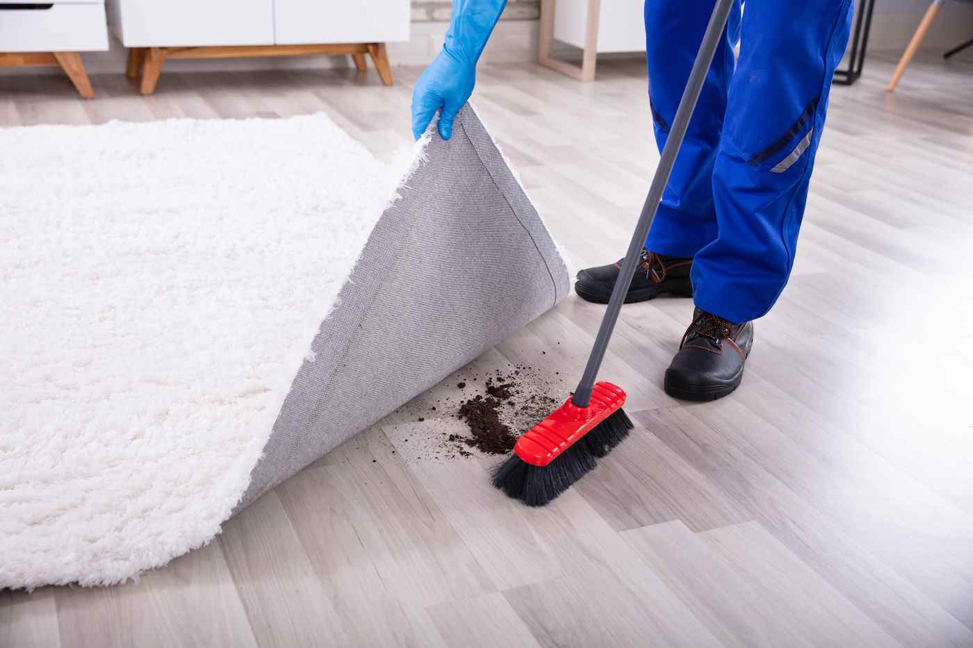 Vue en coupe basse d'un concierge nettoyant la saleté sous le tapis avec une vadrouille