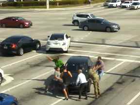 Un groupe de passants aide à arrêter un véhicule à une intersection achalandée après qu'une femme a eu un épisode médical à Boynton Beach, en Floride.