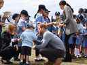 Le prince Harry, au centre, se fait chatouiller la barbe par Luke Vincent, élève de l'école publique de Buninyong, alors que sa femme Meghan, la duchesse de Sussex, salue ses camarades après leur arrivée à l'aéroport régional de Dubbo à Dubbo le 17 octobre 2018. (DEAN LEWINS/AFP/Getty Images)