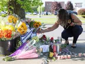 Une personne en deuil s'accroupit devant des fleurs et des bougies, lors d'une veillée pour les victimes de la fusillade dans un supermarché TOPS à Buffalo, NY, le dimanche 15 mai 2022.