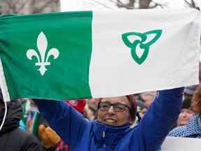 Une femme brandit le drapeau franco-ontarien devant l'édifice des droits de la personne lors de la Journée d'action franco-ontarienne à Ottawa, Ontario, le 1er décembre 2018.