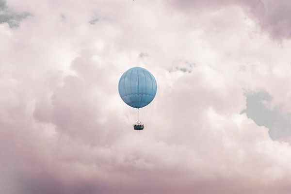 une photo d'un ballon à air chaud bleu contre un ciel nuageux rose