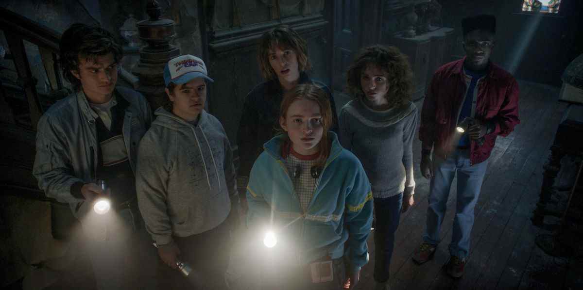 Le gang Hawkins dans Stranger Things saison 4 regardant vers la caméra dans une maison hantée