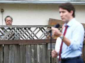 Un homme regarde le premier ministre du Canada Justin Trudeau s'entretenir avec des journalistes à l'extérieur d'une maison où il a rencontré des résidents pour discuter des investissements fédéraux dans le logement, à Vancouver, Colombie-Britannique, Canada, le 24 mai 2022. PHOTO PAR