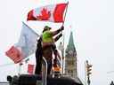 Des gens agitent des drapeaux au sommet d'un camion devant la Colline du Parlement à Ottawa, le 6 février 2022, lors de la manifestation des camionneurs du Freedom Convoy contre les mandats de vaccination et d'autres mesures COVID.