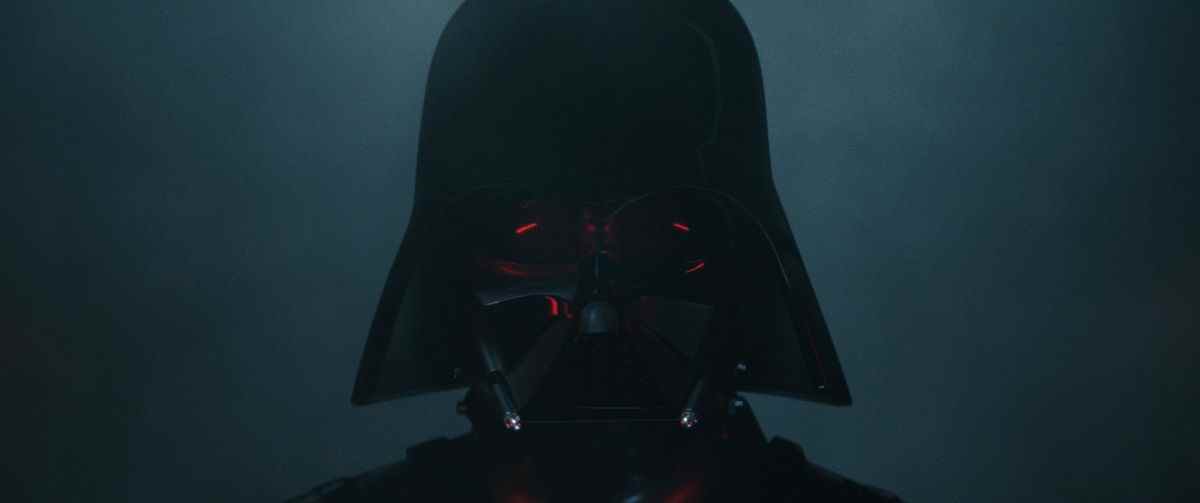 Dark Vador se tient dans l'obscurité, son casque reflétant subtilement la lumière de son sabre laser en Obi-Wan Kenobi. 