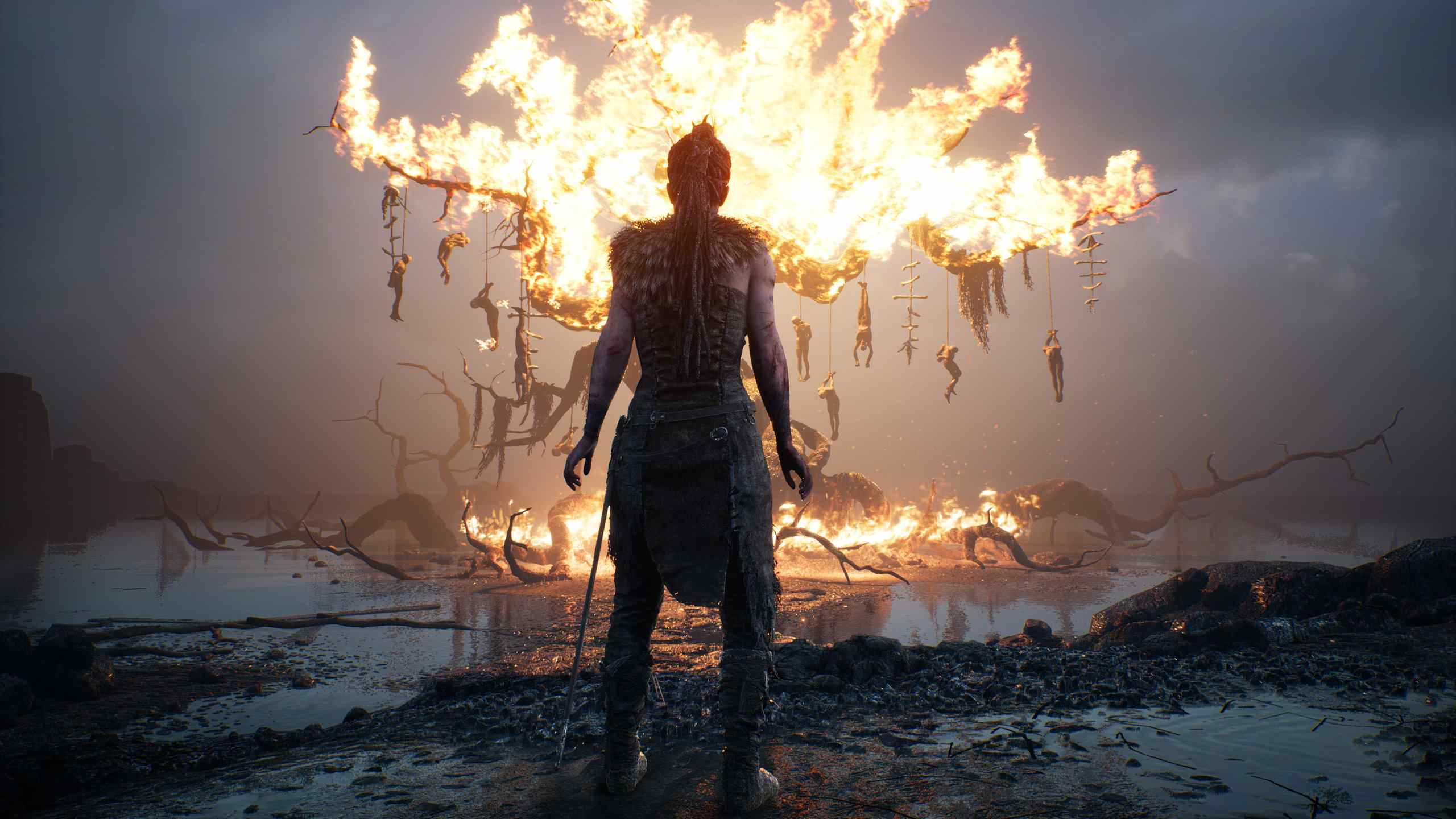 Senua se tient devant un arbre en feu avec des cadavres suspendus dans une capture d'écran de Hellblade.