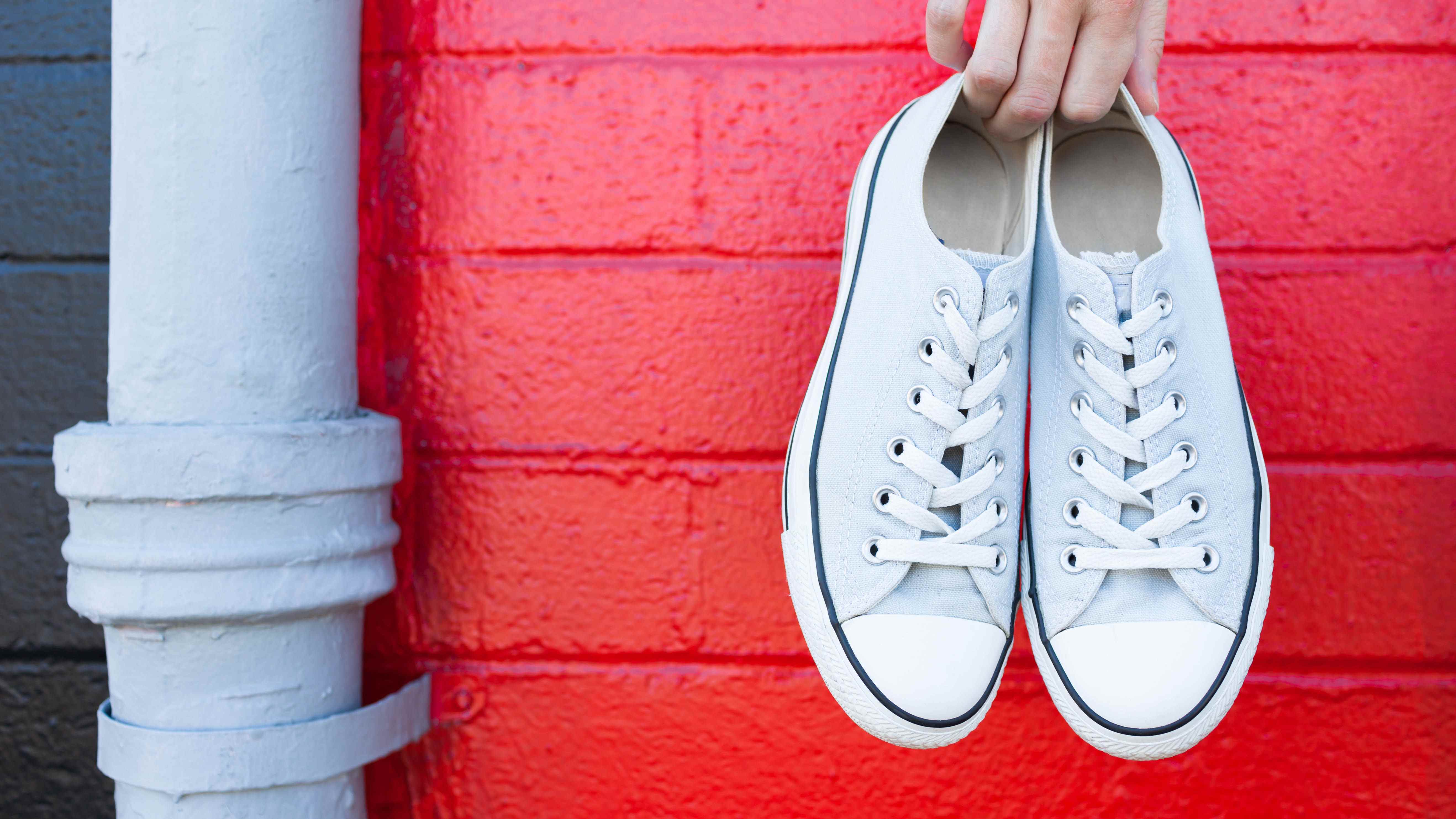 Une paire de chaussures blanches tenue sur un mur rouge