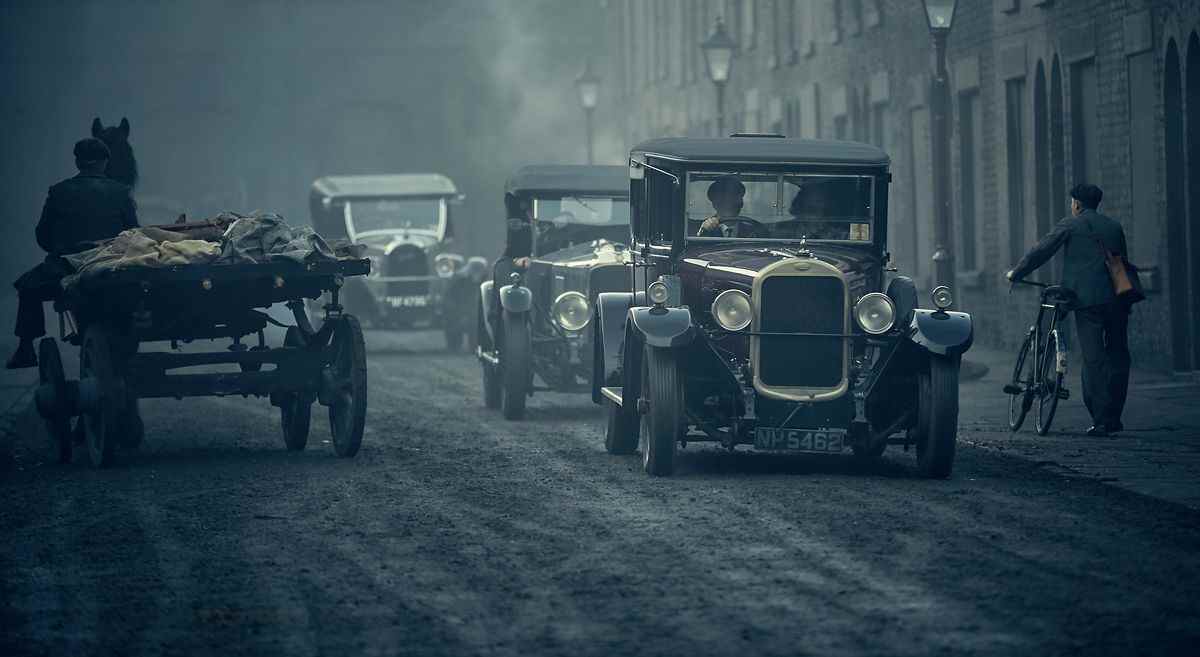 Les Peaky Blinders conduisant une voiture à distance, croisant un homme promenant un vélo et une calèche