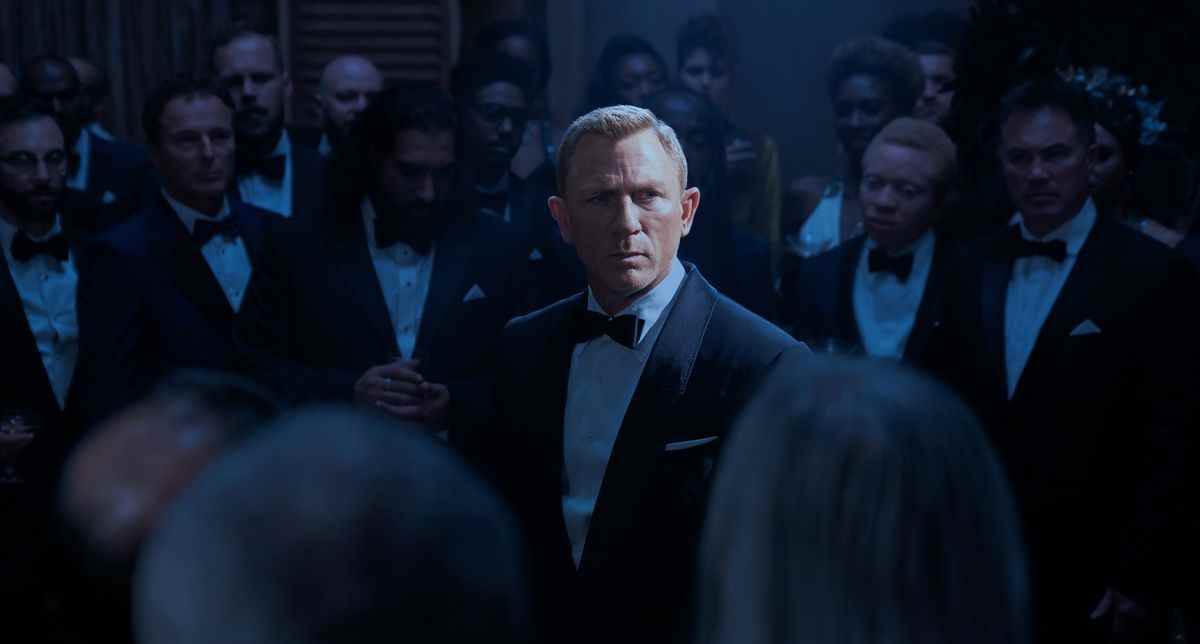 Daniel Craig dans le rôle de James Bond dans No Time to Die, sous les projecteurs, entouré de membres de SPECTRE en costume formel