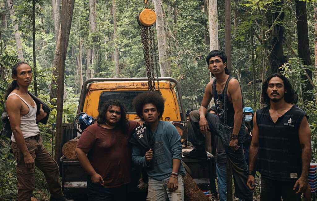 Cinq individus debout derrière un camion à plateau dans la jungle.