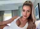 Paige Spiranac allongée sur un lit en body blanc.