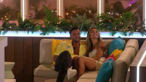 davide et ekin su de love island sourient en s'asseyant ensemble sur le canapé à l'extérieur