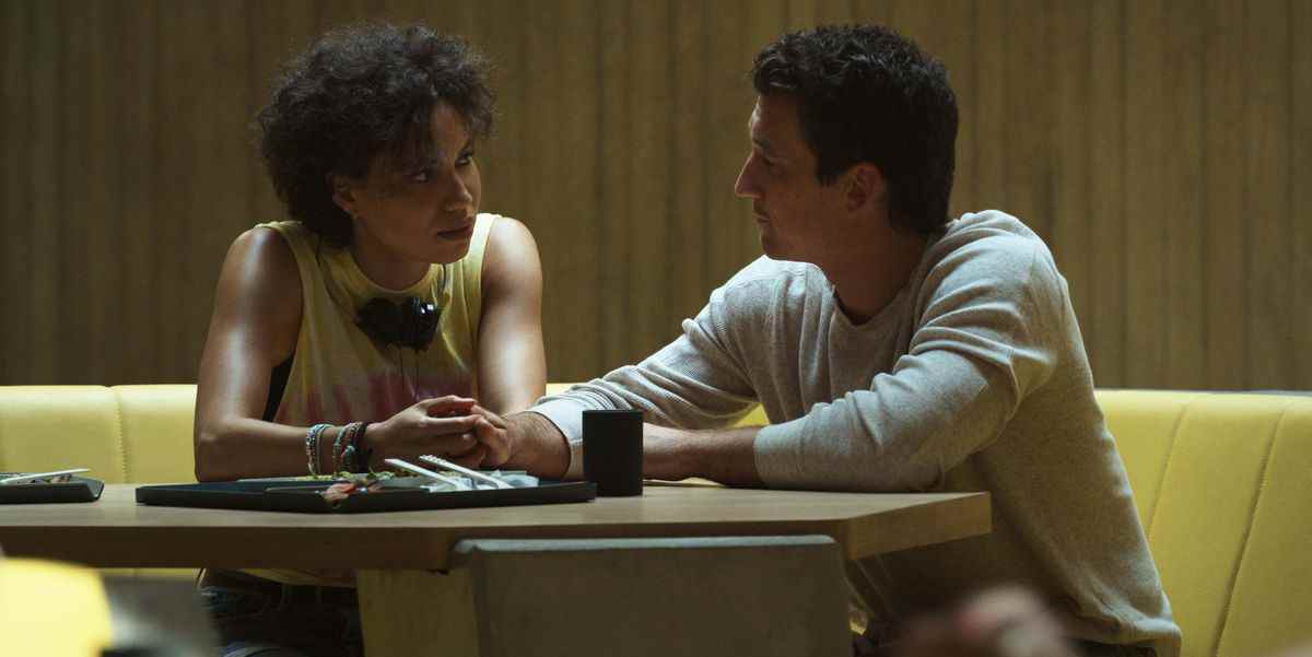 Jurnee Smollett et Miles Teller sont assis ensemble à une table, se touchant les mains, dans la prison de Spiderhead dans Spiderhead de Netflix