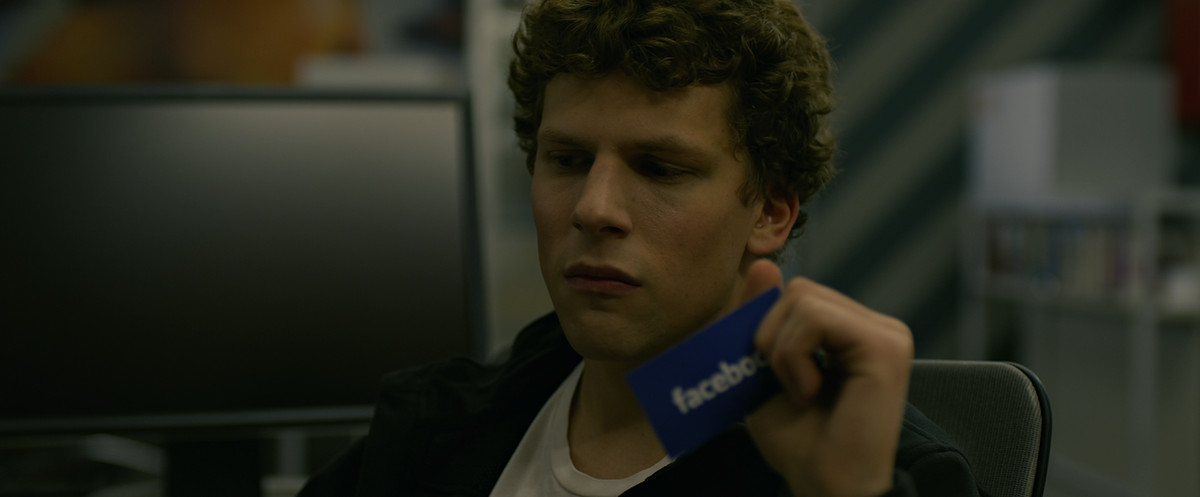 Jesse Eisenberg tient une carte avec le logo Facebook dans The Social Network.