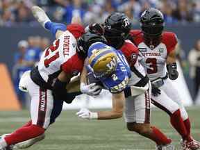 Greg Ellingson (2) des Blue Bombers de Winnipeg est plaqué par Justin Howell (21) et Sherrod Baltimore (27) des Redblacks d'Ottawa lors de la première moitié de l'action de la LCF à Winnipeg, le vendredi 10 juin 2022.