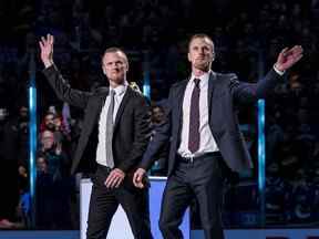 Les anciens joueurs des Canucks de Vancouver, Daniel Sedin et Henrik Sedin, de Suède, réagissent lors d'une cérémonie de départ à la retraite tenue avant un match entre les Canucks de Vancouver et les Blackhawks de Chicago au Rogers Arena.