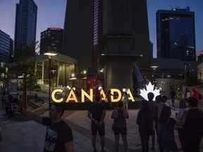 Les visiteurs se rassemblent près d'une enseigne illuminée du Canada à l'extérieur de la Tour CN à Toronto.