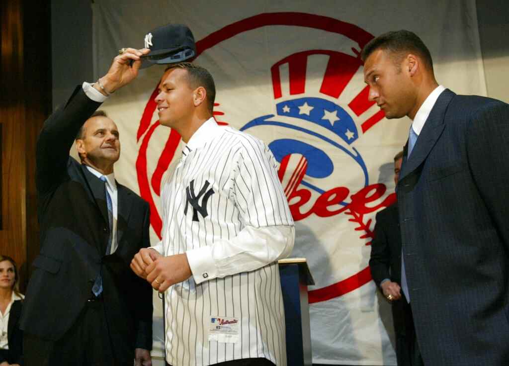 DOSSIER – Dans cette photo d'archive du 17 février 2004, le skipper des Yankees de New York, Joe Torre, met une casquette des Yankees sur le nouveau membre de l'équipe Alex Rodriguez alors que son coéquipier Derek Jeter regarde lors d'une conférence de presse sur le baseball au Yankee Stadium de New York.  Trois prix MVP, 14 sélections All-Star, deux contrats record et d'innombrables controverses plus tard, A-Rod est la cible la plus importante et la plus riche d'une enquête sur les drogues améliorant la performance, avec une décision du commissaire au baseball Bud Selig attendue lundi, 5 août 2013. (AP Photo/Gregory Bull, File)