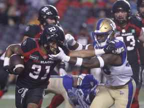 Le porteur de ballon Devonte Williams (31 ans) des Redblacks d'Ottawa est attaqué par le demi défensif des Blue Bombers de Winnipeg Donald Rutledge Jr (38 ans) lors de la première mi-temps de l'action de la LCF au stade TD Place à Ottawa le vendredi 17 juin 2022.