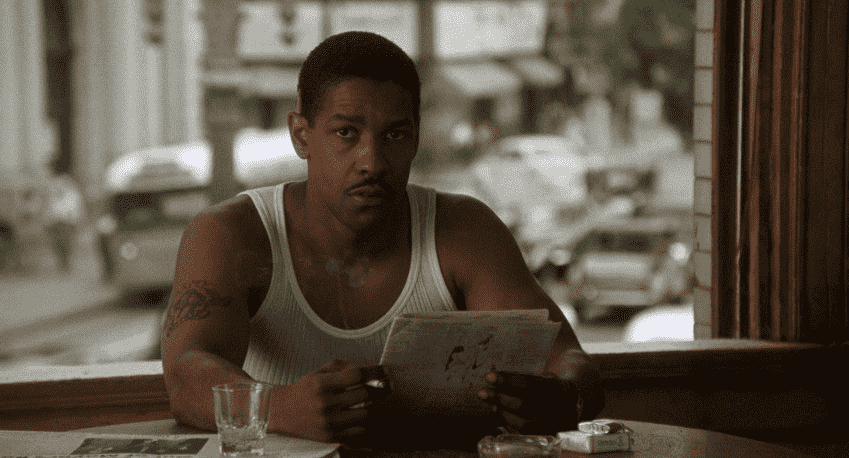 Denzel Washington, vêtu d'un débardeur blanc, lit le journal dans Devil in a Blue Dress.