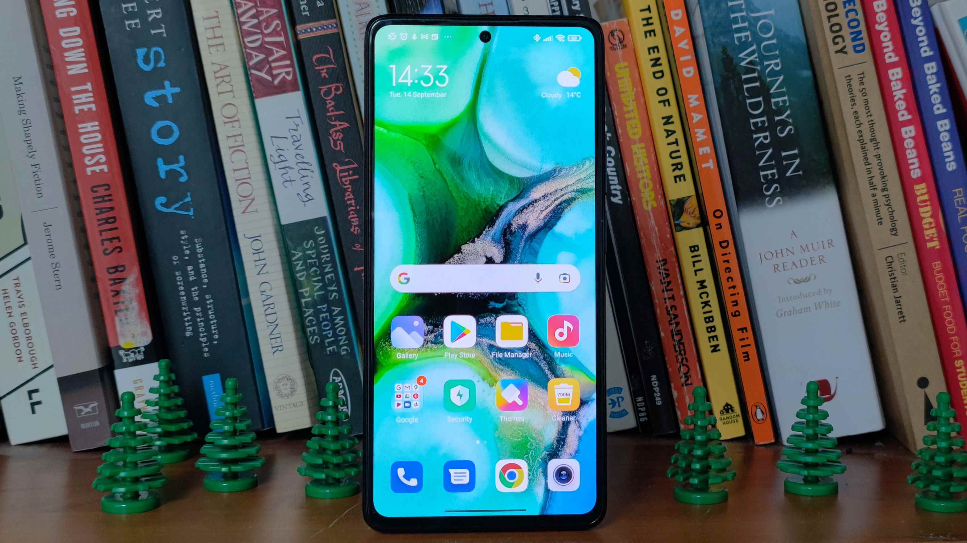 Un Xiaomi 11T Pro devant des livres, flanqué d'arbres en plastique