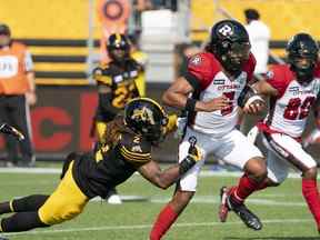 Le quart-arrière des Redblacks d'Ottawa Caleb Evans (5) est attaqué par le demi défensif des Tiger Cats de Hamilton Tunde Adeleke (2) au cours de la première moitié de l'action de football de la LCF à Hamilton, en Ontario.  le samedi 16 juillet 2022.