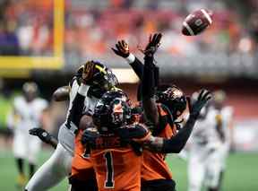 Emmanuel Butler des Tiger-Cats de Hamilton, arrière gauche, et Jordan Williams des Lions de la Colombie-Britannique, arrière droit, se disputent le ballon avant que Garry Peters (1) ne fasse l'interception lors du dernier jeu du match au cours de la seconde moitié du match de football de la LCF en Vancouver, le jeudi 21 juillet 2022.