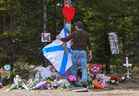 Un homme ajuste le drapeau de la Nouvelle-Écosse devant le mémorial de fortune, fabriqué à la mémoire des victimes d'une fusillade de masse à Portapique, en Nouvelle-Écosse, le 23 avril 2020. 