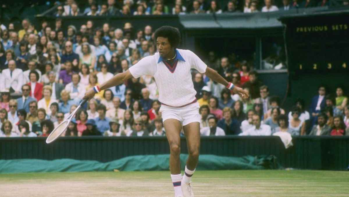 Arthur Ashe frappe un revers sur un court de tennis sous les yeux de la foule.