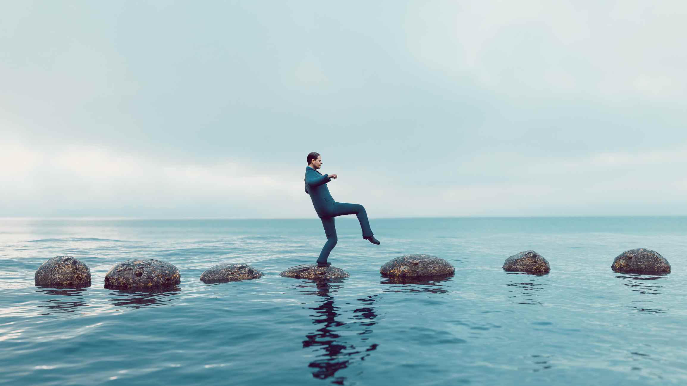 L'homme marche prudemment sur un chemin de petits rochers au milieu de la mer ;  le capital-investissement doit faire preuve de prudence face aux sanctions