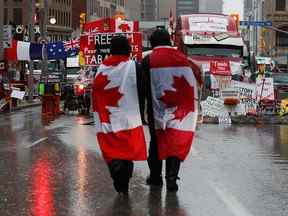 Les gens marchent avec des drapeaux canadiens près des panneaux de soutien au Freedom Convoy, alors que les camionneurs et les partisans protestent contre les mandats de vaccination et d'autres mesures COVID à Ottawa le 17 février 2022.