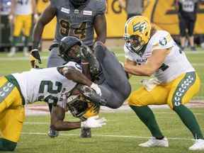 Le demi défensif des Tiger Cats de Hamilton Lawrence Woods (37) est attaqué par le demi défensif des Elks d'Edmonton Mike Dubuisson (29) et Ante Milanovic-Litre (34) lors de la première mi-temps du match de football de la LCF à Hamilton, en Ontario, le vendredi 1er juillet 2022 .