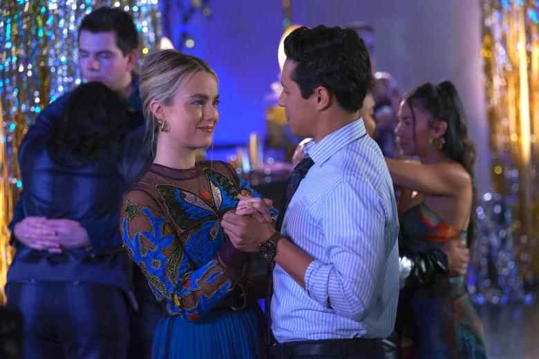 A blonde woman with pulled back hair and a blue and red butterfly-patterned dress dances with a man in a light blue collared shirt in a high school gym; still from "Maggie."