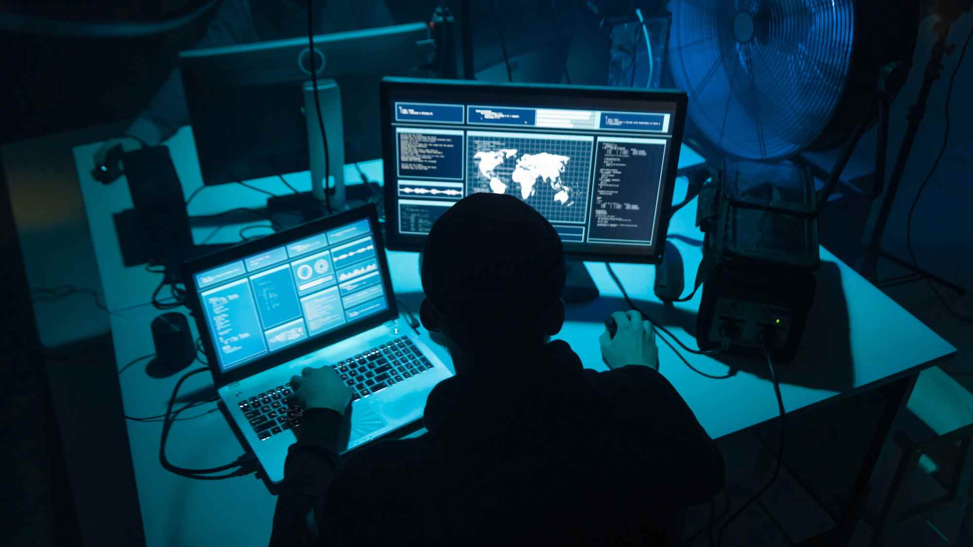 homme assis à un bureau sombre travaillant sur un ordinateur portable et un ordinateur de bureau