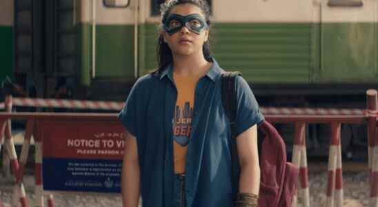 A teen girl in an orange tee and blue shirt, wearing a matching blue mask over her eyes, stands outside a train in Pakistan; still from "Ms. Marvel"