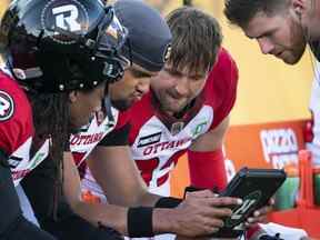 Le quart-arrière des Redblacks d'Ottawa Caleb Evans, au centre, regarde les rediffusions de matchs lors de la première mi-temps d'un match de football de la LCF contre les Tiger Cats de Hamilton à Hamilton, en Ontario.  le samedi 16 juillet 2022.