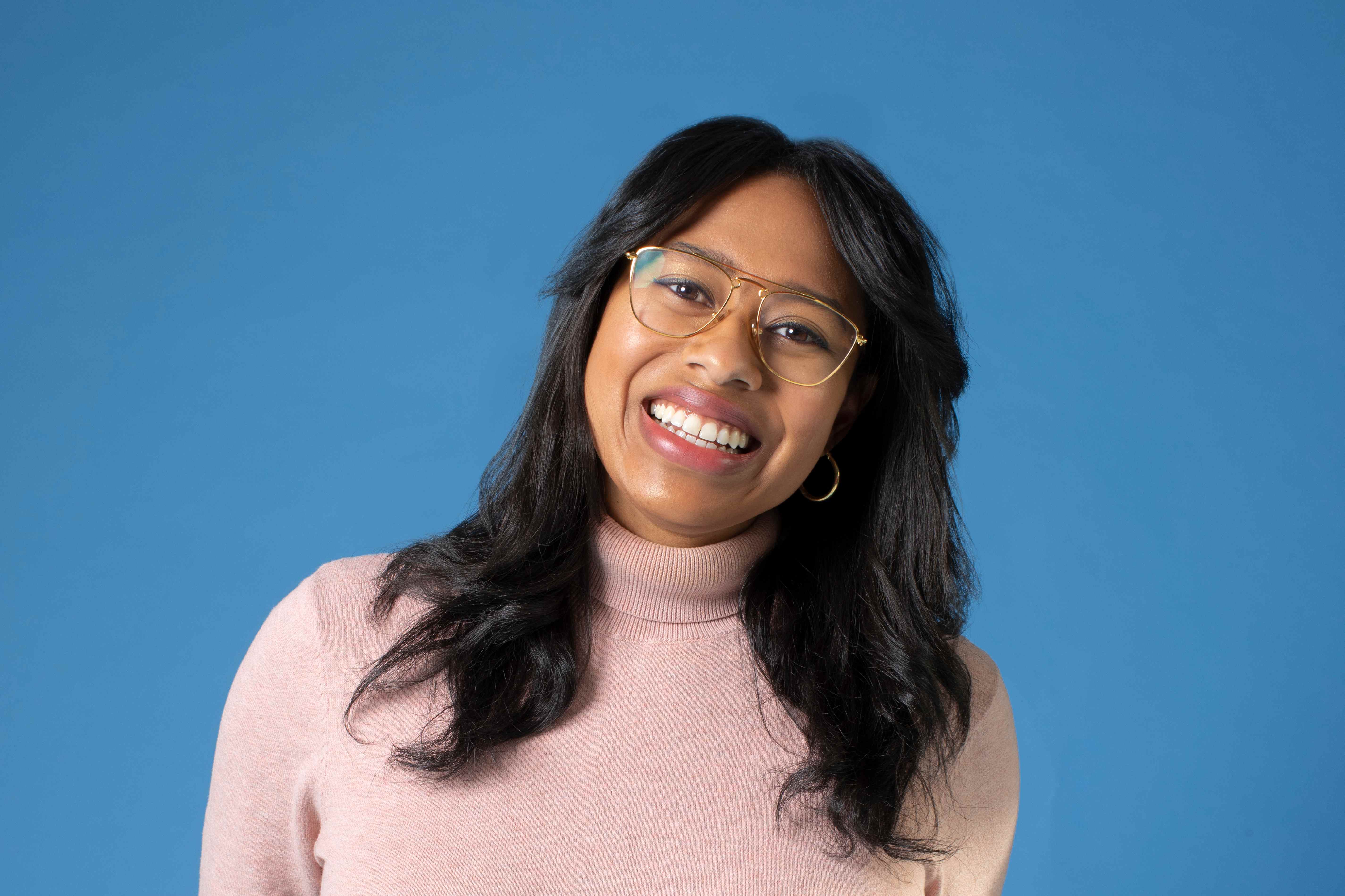 Pilar Johnson sourit à la caméra avec des lunettes et un col roulé rose