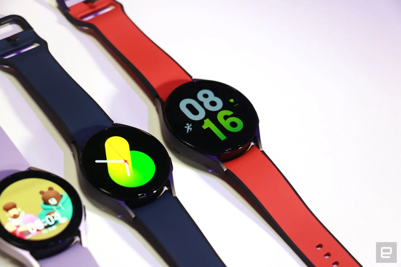 Un trio d'unités Galaxy Watch 5 sur une table, avec des bracelets violets, bleus et rouges de gauche à droite.