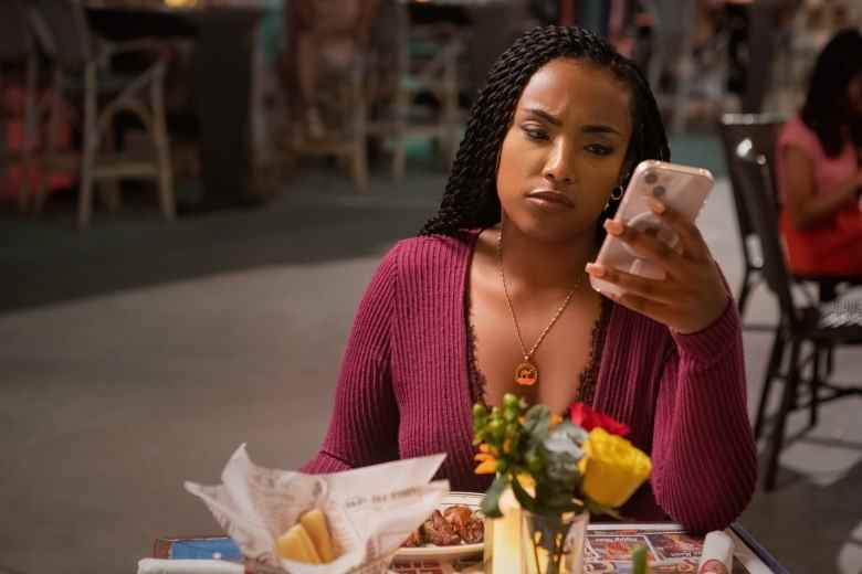 A young woman in a magenta top checks her phone while eating outdoors.