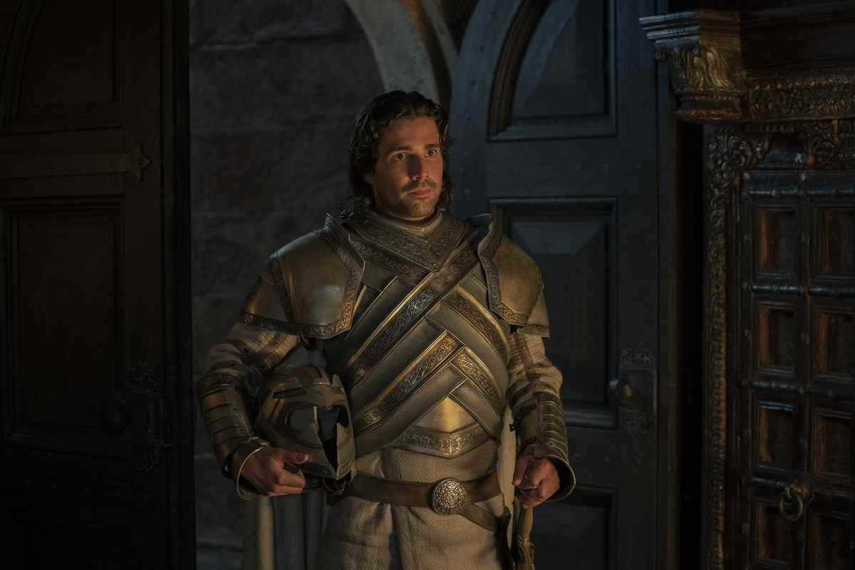 Ser Criston Cole se tient à l'entrée d'une pièce portant son armure de chevalier et tenant son casque dans House of the Dragon.